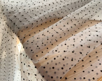 May include: White tulle fabric with black polka dots. The fabric is sheer and has a delicate texture.