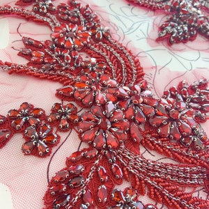 May include: Red beaded and sequined appliqué with a floral design. The appliqué is made with small red beads and sequins, and it has a delicate floral pattern. The appliqué is perfect for adding a touch of sparkle and elegance to any garment.