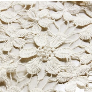 May include: Close-up of a white crocheted lace fabric with a delicate floral pattern.