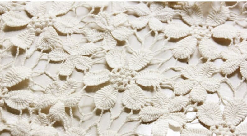 May include: Close-up of a white crocheted lace fabric with a delicate floral pattern.