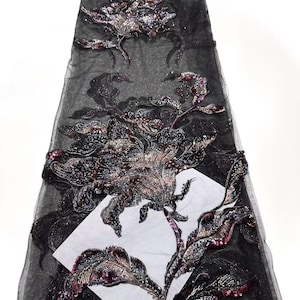May include: Black floral embroidered fabric with sequins and beads. The design features large, detailed flowers and leaves in shades of black, silver, and burgundy. The fabric is a sheer black mesh, and the embroidery is dense and intricate.