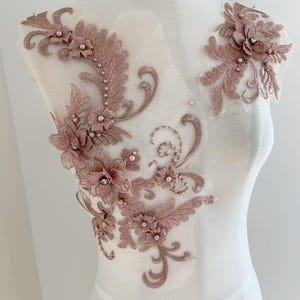 May include: Dusty rose floral lace appliqué with pearl and rhinestone accents. The appliqué features detailed embroidery of flowers and leaves, ideal for embellishing bridal wear or other garments.