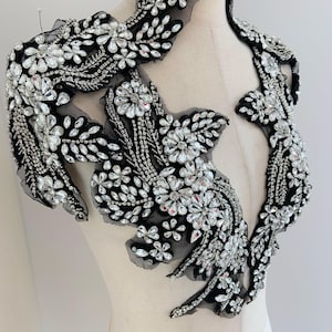 May include: A black mesh applique with a floral design embellished with clear rhinestones. The applique is perfect for adding a touch of sparkle to any garment.