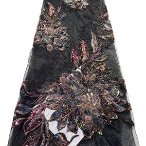 Op de afbeelding: Zwarte kanten stof met uitgebreide bloemenborduurwerk. Het ontwerp toont grote, gedetailleerde bloemen in tinten bruin, rood en blauw, versierd met kralen en pailletten. De stof is doorschijnend, met een delicate, open weefsel.