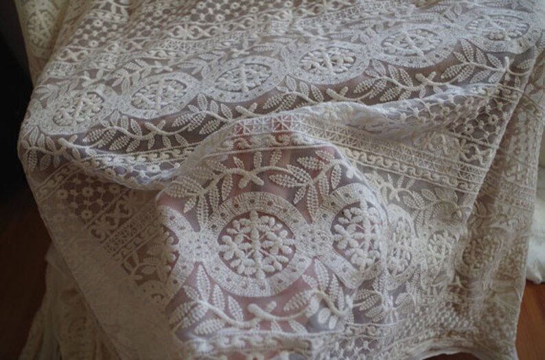 Puede incluir: Tela de encaje blanca con un intrincado patr&oacute;n floral. La tela es transparente y delicada, con una textura suave y fluida.