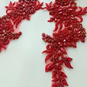 May include: Two red beaded lace appliques with a floral design and red rhinestones. The appliques are on a white background.