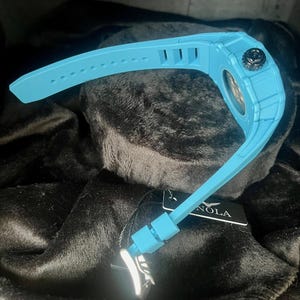 May include: A light blue wristwatch with a black crown and a matching light blue band. The watch has a textured case and a tag with the word "NOLA" on it.