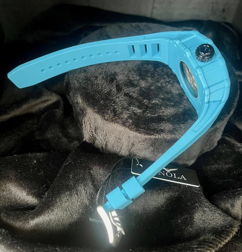 May include: A light blue wristwatch with a black crown and a matching light blue band. The watch has a textured case and a tag with the word "NOLA" on it.