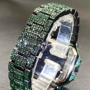 May include: A luxury watch band with a black frame and a dazzling array of emerald-green gemstones. The band is made of rectangular links, each covered in sparkling green stones. The watch face is silver, and the overall design is elegant and eye-catching.