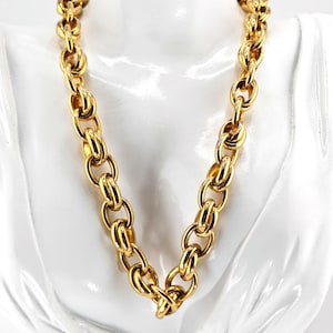 May include: A gold-colored chain necklace with large oval links. The necklace is displayed on a white bust. The chain is thick and appears to be made of metal. The links are closely connected, creating a bold and stylish accessory.
