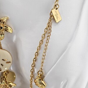 May include: Gold-toned necklace with seashell and starfish charms. The necklace features a delicate chain and a small tag with the brand name. The charms are detailed and add a coastal theme to the jewelry.