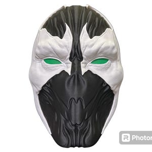 May include: A full-face mask featuring a high-contrast design with a black lower section and white upper section. The mask has textured, organic-looking contours and bright green mesh inserts covering the eye openings, creating a striking appearance.