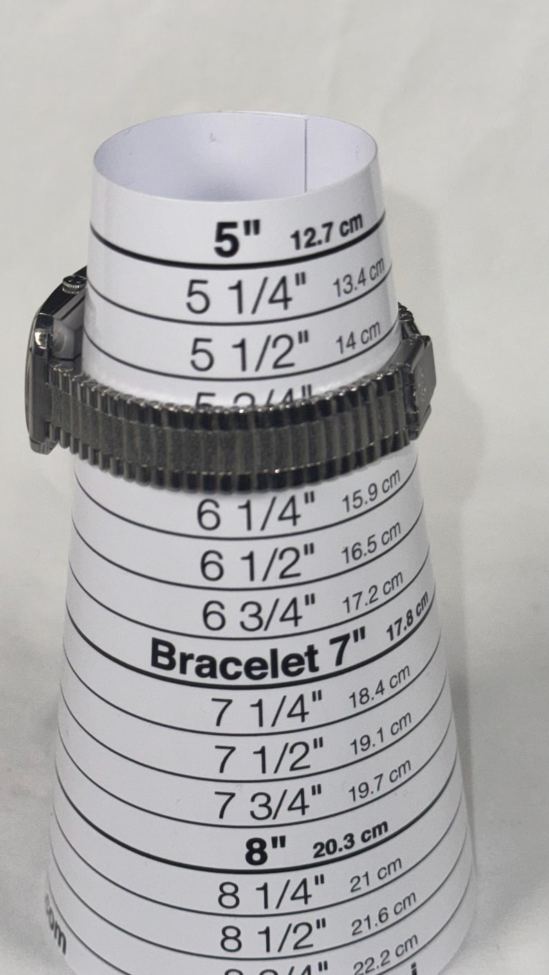 May include: A silver-toned watch bracelet is placed on a white bracelet sizing cone. The cone displays measurements from 5" (12.7 cm) to 8 3/4" (22.2 cm), with both inches and centimeters. The text "Bracelet 7" is visible.