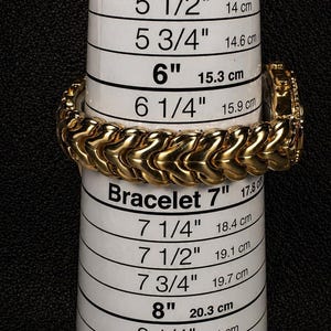 May include: A gold-colored bracelet with a textured design is displayed on a white measuring tool. The tool has measurements in inches and centimeters, ranging from 5 inches (12.7 cm) to 8 3/4 inches (22.2 cm). The text "EZ Bracelet Mini" is visible.