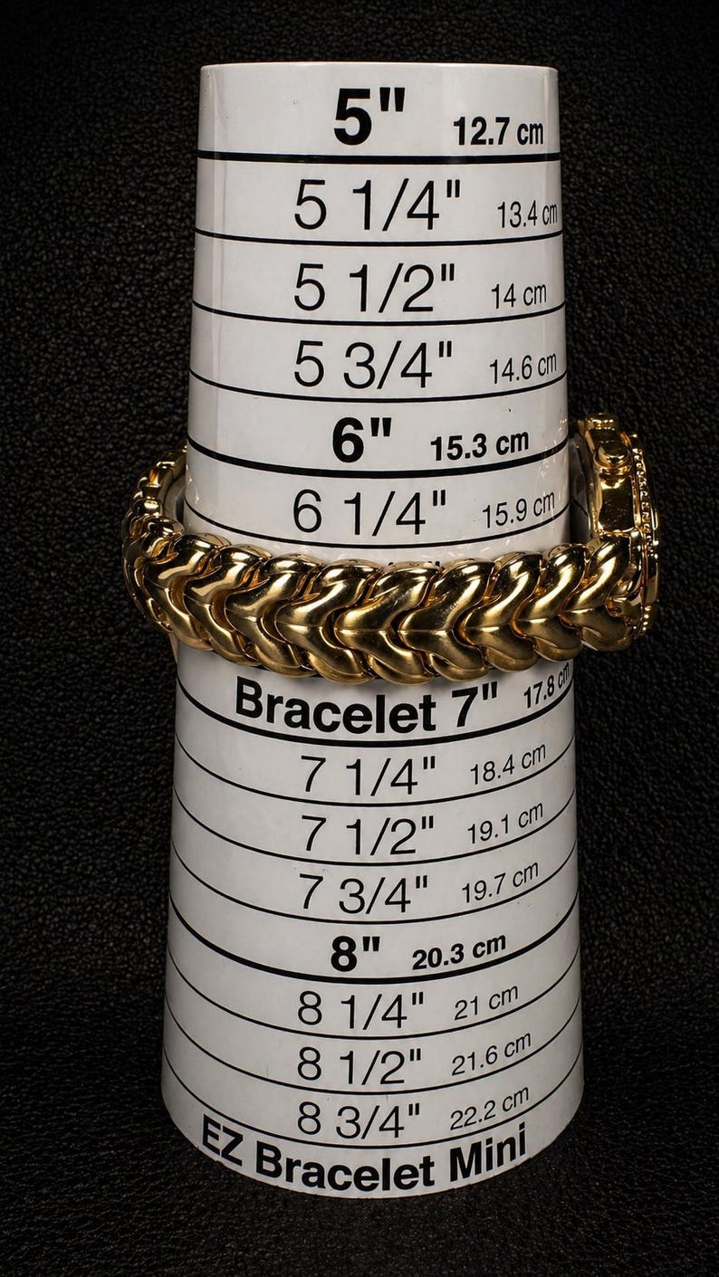 May include: A gold-colored bracelet with a textured design is displayed on a white measuring tool. The tool has measurements in inches and centimeters, ranging from 5 inches (12.7 cm) to 8 3/4 inches (22.2 cm). The text "EZ Bracelet Mini" is visible.