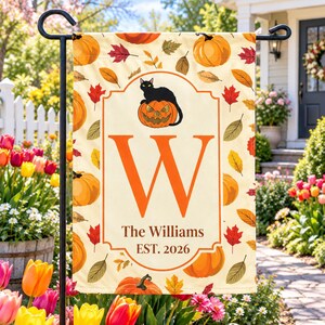 May include: A rectangular garden flag featuring a cream background with a pattern of orange pumpkins and autumn leaves. A central orange frame contains a black cat sitting on a jack-o'-lantern, a large orange letter W, and the text The Williams EST. 2026.