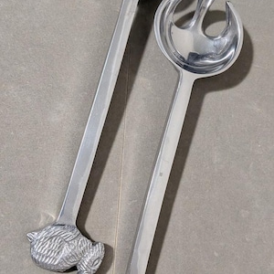 Peut inclure: Une paire d'ustensiles de service à salade en métal argenté dotés de longs manches droits se terminant par des embouts détaillés et texturés en forme de lapin. L'un est une cuillère ronde pleine, l'autre une fourchette à salade fendue.
