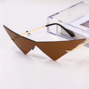 May include: Brown, geometric-shaped sunglasses with gold-colored metal arms and a black bridge. The lenses have a sharp, angular design. The sunglasses are a unique fashion accessory.
