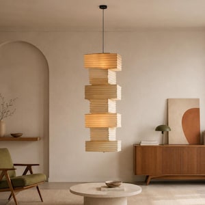May include: A vertical pendant light fitting featuring a series of stacked, rectangular, off-white paper-like shades. The structure is suspended by a thin black cord from the ceiling, creating a layered, geometric column that emits a warm glow.