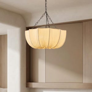 May include: A bowl-shaped pendant light fixture featuring a cream-colored fabric shade with vertical pleats and dark metal piping along the edges. The light is suspended from the ceiling by a dark metal chain that branches into three support arms.