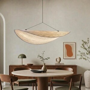 May include: A contemporary pendant light with a layered, organic form hangs above a round dining table. The room has a neutral colour scheme, with a wooden sideboard and artwork. The light fixture is a key design element.
