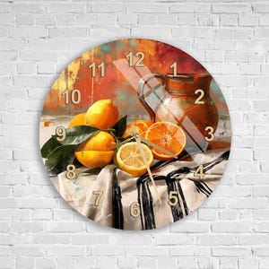 May include: A round wall clock featuring a still life painting of lemons, an orange slice, and a ceramic pitcher on a white cloth with black stripes. The clock face displays numbers 1 through 12 in a light color, with thin gold-toned clock hands.