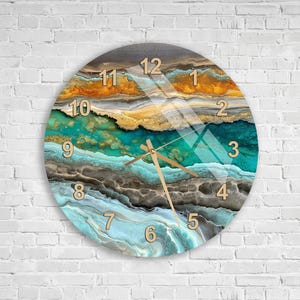 May include: A round wall clock featuring a fluid abstract design with layered bands of teal, gold, brown, and white. The clock face displays gold-colored numerals from 1 to 12 and three thin gold-colored hands indicating the time against the pattern.