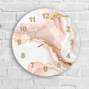 Könnte beinhalten: Runde Wanduhr mit Marmormuster in Rosa, Weiß und Gold. Das Zifferblatt hat goldene Ziffern und Zeiger. Die Uhr ist an einer weißen Backsteinmauer befestigt.