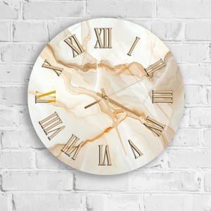 Peut inclure: Horloge murale ronde avec un motif marbré. Le cadran de l'horloge présente un motif crème et or avec des chiffres romains dorés. Les aiguilles de l'horloge sont dorées, et l'horloge est fixée sur un mur de briques blanches.