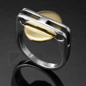 May include: A silver ring with a gold heart-shaped design. The ring has a unique geometric design with two parallel lines.