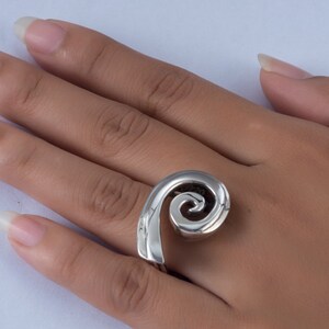 K&ouml;nnte beinhalten: Ein silberner Ring mit einem Spiraldesign. Der Ring wird an einem Finger getragen.