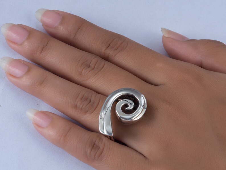 K&ouml;nnte beinhalten: Ein silberner Ring mit einem Spiraldesign. Der Ring wird an einem Finger getragen.