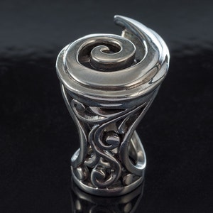 K&ouml;nnte beinhalten: Ein silberner Ring mit einem wirbelnden Design. Der Ring ist mit komplizierten Details gefertigt und hat eine einzigartige, organische Form.