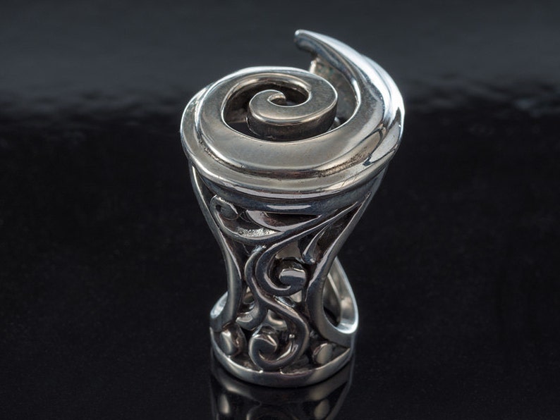 K&ouml;nnte beinhalten: Ein silberner Ring mit einem wirbelnden Design. Der Ring ist mit komplizierten Details gefertigt und hat eine einzigartige, organische Form.