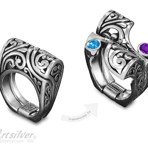 May include: A silver ring with a filigree design. The ring has two gemstones, one blue and one purple. The ring is shown in two positions, one with the gemstones visible and one with the gemstones hidden.