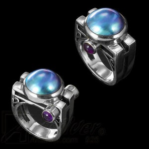 Könnte beinhalten: Zwei Silberringe mit einer blauen, schillernden Perle und einem violetten Edelstein. Die Ringe haben ein geometrisches Design.
