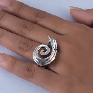 K&ouml;nnte beinhalten: Ein silberner Ring mit einem Spiraldesign. Der Ring wird an einem Finger getragen.