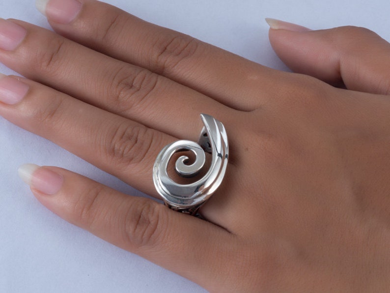 K&ouml;nnte beinhalten: Ein silberner Ring mit einem Spiraldesign. Der Ring wird an einem Finger getragen.