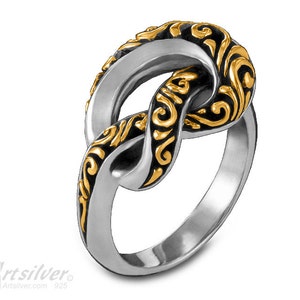 May include: A silver ring with a gold-plated knot design. The knot is intricately detailed with swirling patterns.