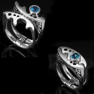 May include: Two silver rings with intricate designs and blue gemstones. The rings are open and have a hinged closure.