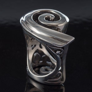 K&ouml;nnte beinhalten: Ein silberner Ring mit einem Spiraldesign. Der Ring besteht aus einem dicken Metallband und hat ein detailliertes, kompliziertes Design.