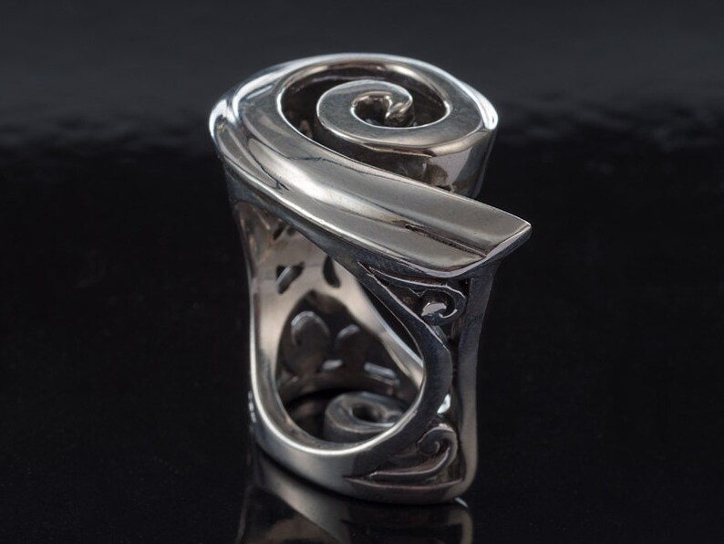 K&ouml;nnte beinhalten: Ein silberner Ring mit einem Spiraldesign. Der Ring besteht aus einem dicken Metallband und hat ein detailliertes, kompliziertes Design.
