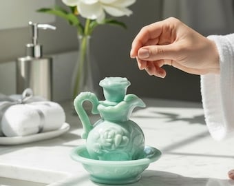 May include: A light green milk glass pitcher and basin set featuring a raised rose floral pattern. The small pitcher has a curved handle and a matching stopper, resting inside a shallow, circular basin with a scalloped edge and embossed details.