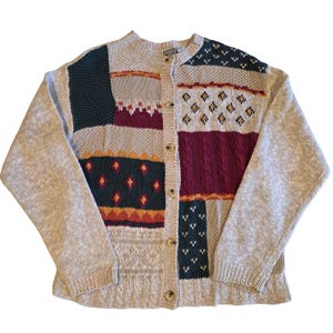 Könnte beinhalten: Eine langärmelige Strickjacke mit Knopfleiste und Patchwork-Design, bestehend aus verschiedenen Strickstrukturen und Mustern in Beige, Dunkelgrün, Burgunderrot und Orange. Das Kleidungsstück hat einen Rundhalsausschnitt und fünf helle Knöpfe.