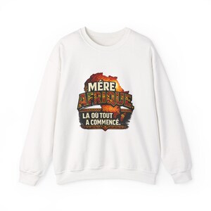 Peut inclure: Sweat-shirt blanc avec un motif coloré du continent africain et les mots "MERE AFRIQUE LA OU TOUT A COMMENCÉ" en noir et or. Le sweat-shirt a des manches longues et un col rond.