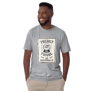 Puede incluir: Una camiseta gris claro con un diseño gráfico rectangular que dice "PREDICT THE FUTURE BY CREATING IT" en un estilo vintage. El diseño incluye un ojo y un diseño de bola de cristal. La camiseta la lleva una persona.