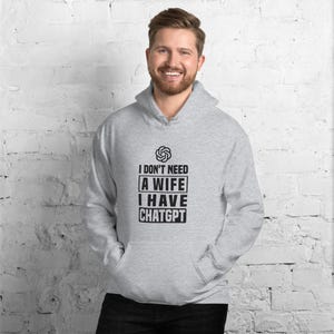 Puede incluir: Una sudadera con capucha gris claro con el texto "I DON'T NEED A WIFE I HAVE CHATGPT" en negro. La sudadera tiene una capucha con cordón y un bolsillo delantero. La persona de la imagen está sonriendo.