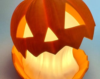 May include: A bright orange jack-o'-lantern lamp with a carved face featuring triangular eyes and a nose. The top section is lifted to reveal a glowing white interior light source, creating a warm illumination that shines through the cutouts.