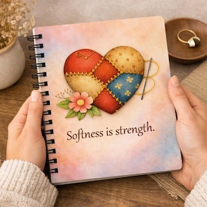 May include: Spiral-bound notebook featuring a patchwork heart design in red, yellow, and blue. A needle and thread are stitched around the heart. The notebook has the text "Softness is strength."