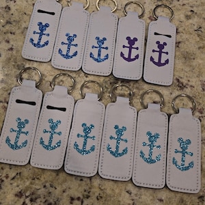 Könnte beinhalten: Eine Sammlung hellgrauer Schlüsselanhänger mit glitzerndem Ankerdesign. Einige Anker sind blau, andere lila. Jeder Schlüsselanhänger hat einen silbernen Schlüsselring.